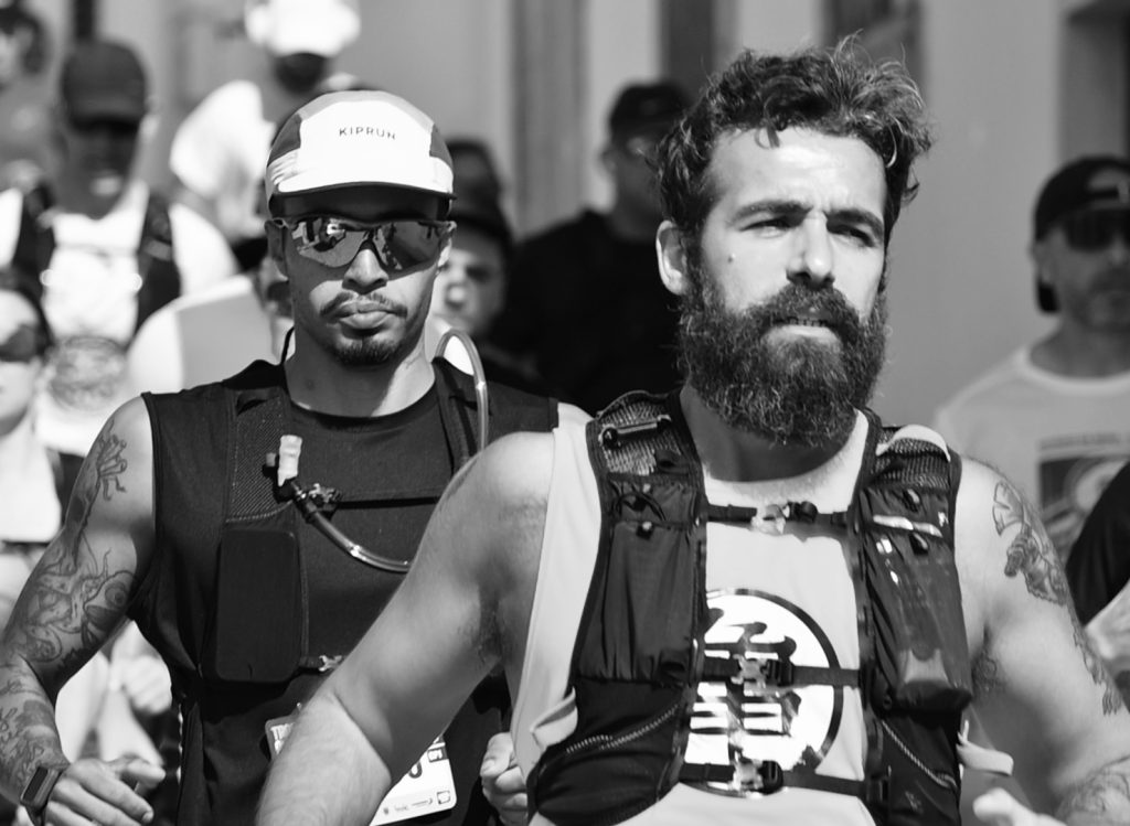 Two runners with the second looking over the shoulder of the first.