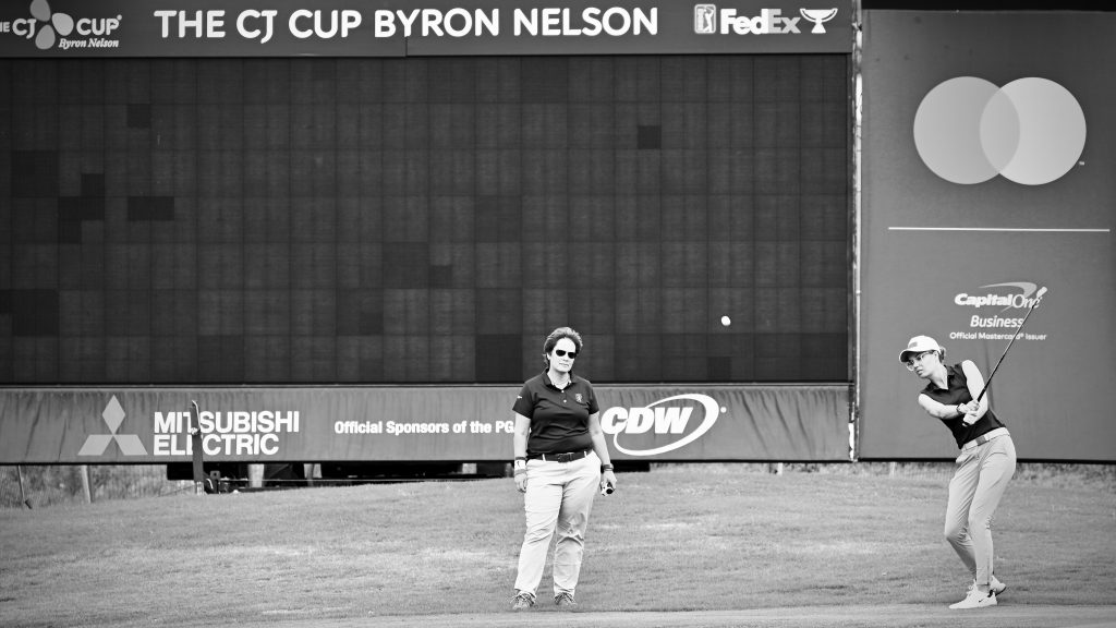 Black-and-white photograph of a woman golfer playing a pitch with her coach looking on.