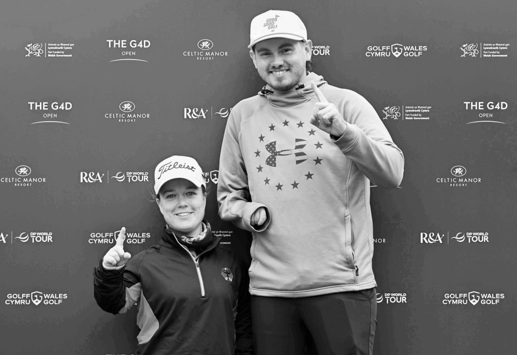 Black-and-white photograph of two G4D golfers smiling and signalling victory in front of The G4D Open sponsor backdrop.